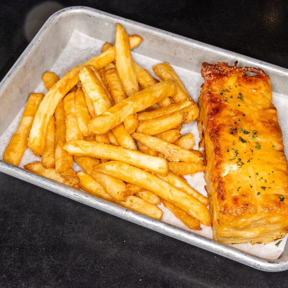Golden fries and a glazed, herb-topped salmon fillet served in a parchment-lined metal tray.