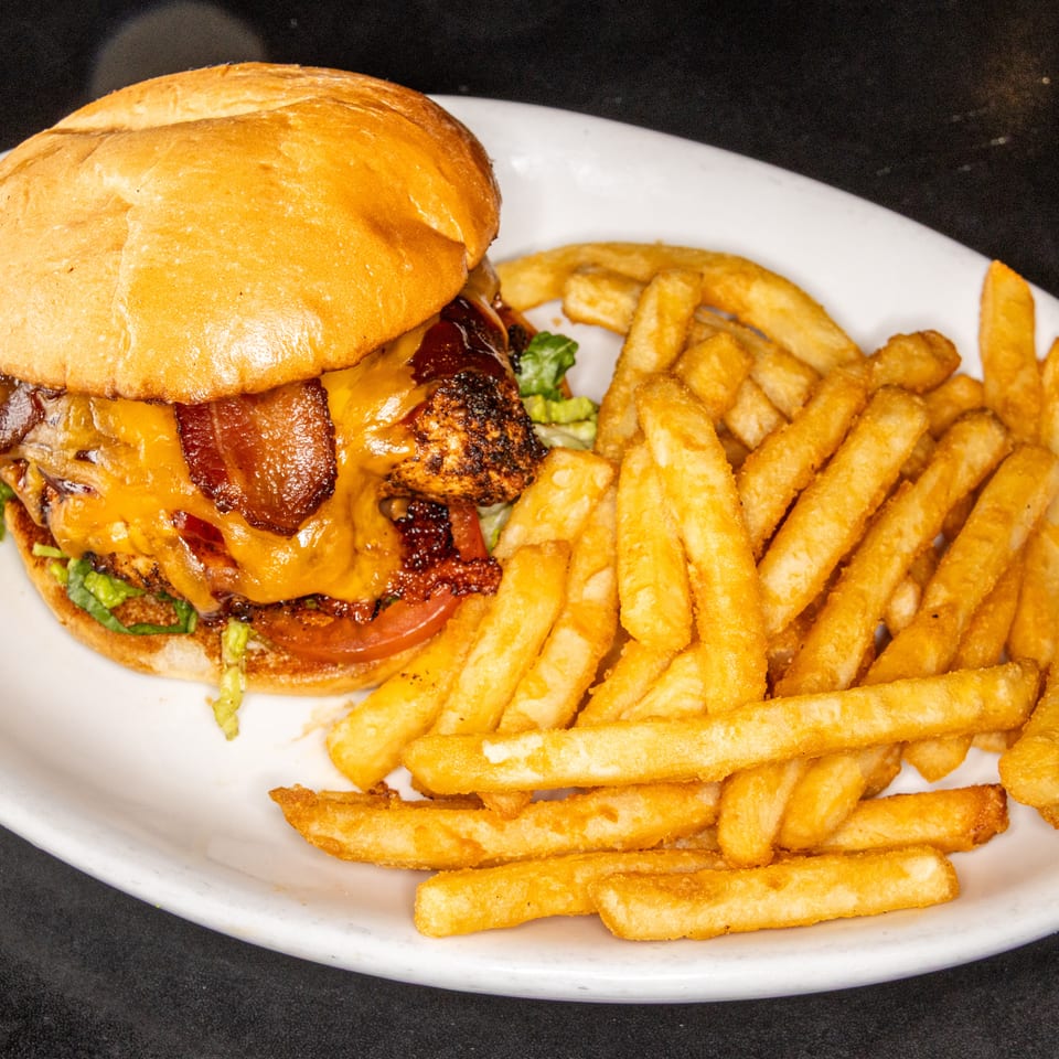 Bacon cheeseburger with lettuce and tomato served alongside golden French fries on a white plate.