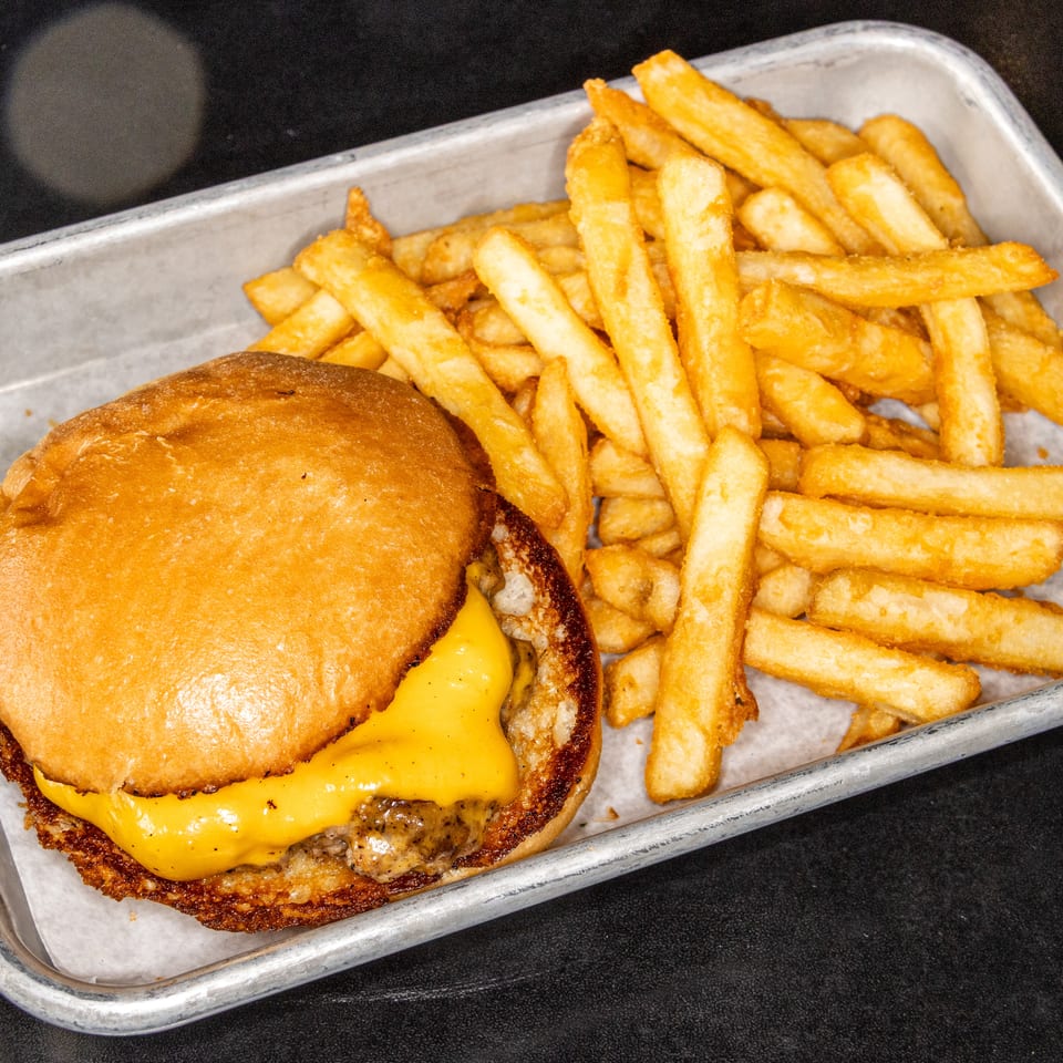 Cheeseburger with melted cheddar and golden fries served on a paper-lined metal tray.