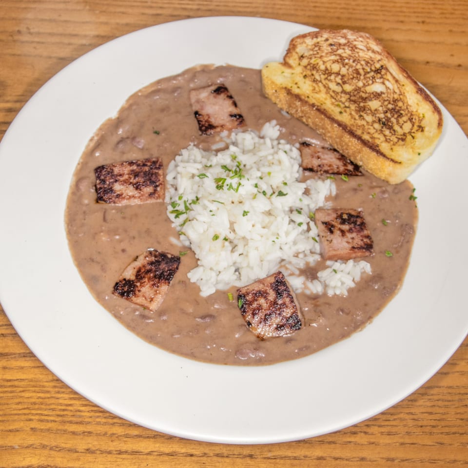 Plate of white rice and grilled meat pieces in creamy beans, served with toasted garlic bread on a wooden table.