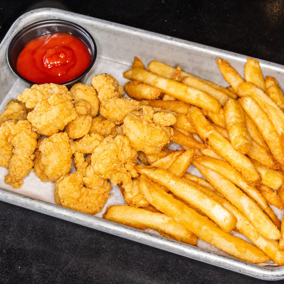 Basket of crispy fried chicken pieces and golden French fries with a cup of ketchup.