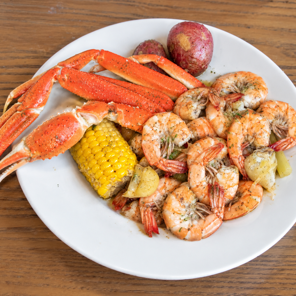 Plate of seasoned snow crab legs, shrimp, corn, red potatoes, and lemon wedges on a wooden table.