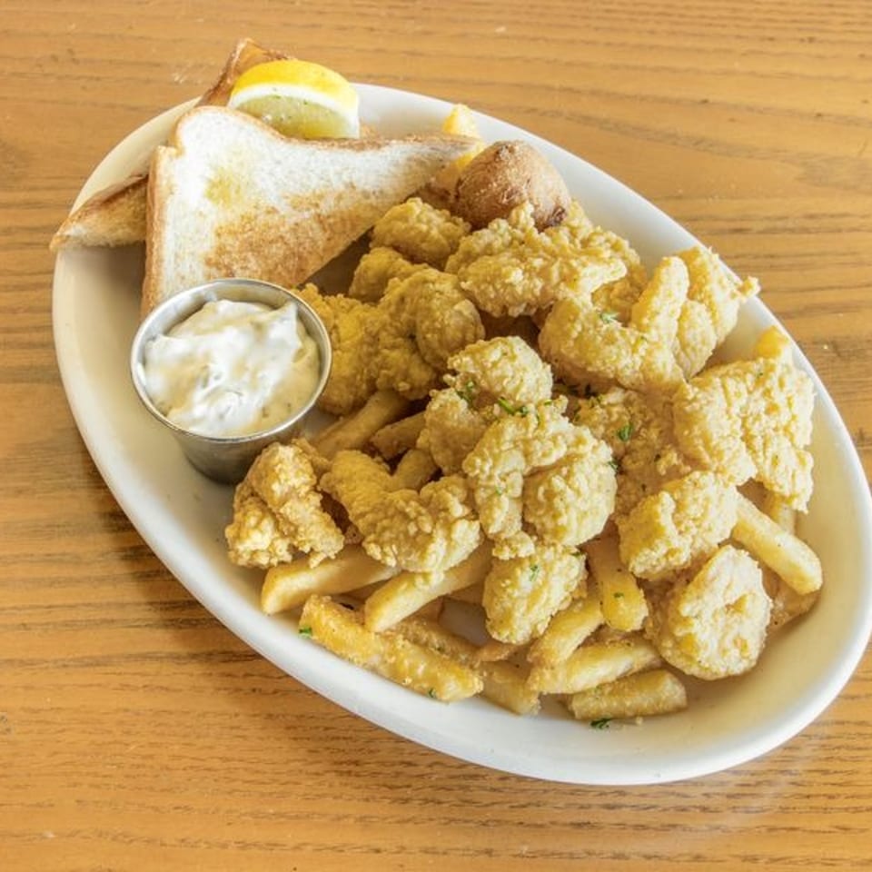 Plate of golden fried calamari and fries with tartar sauce, toast, lemon wedges, and a croquette on a wooden table.