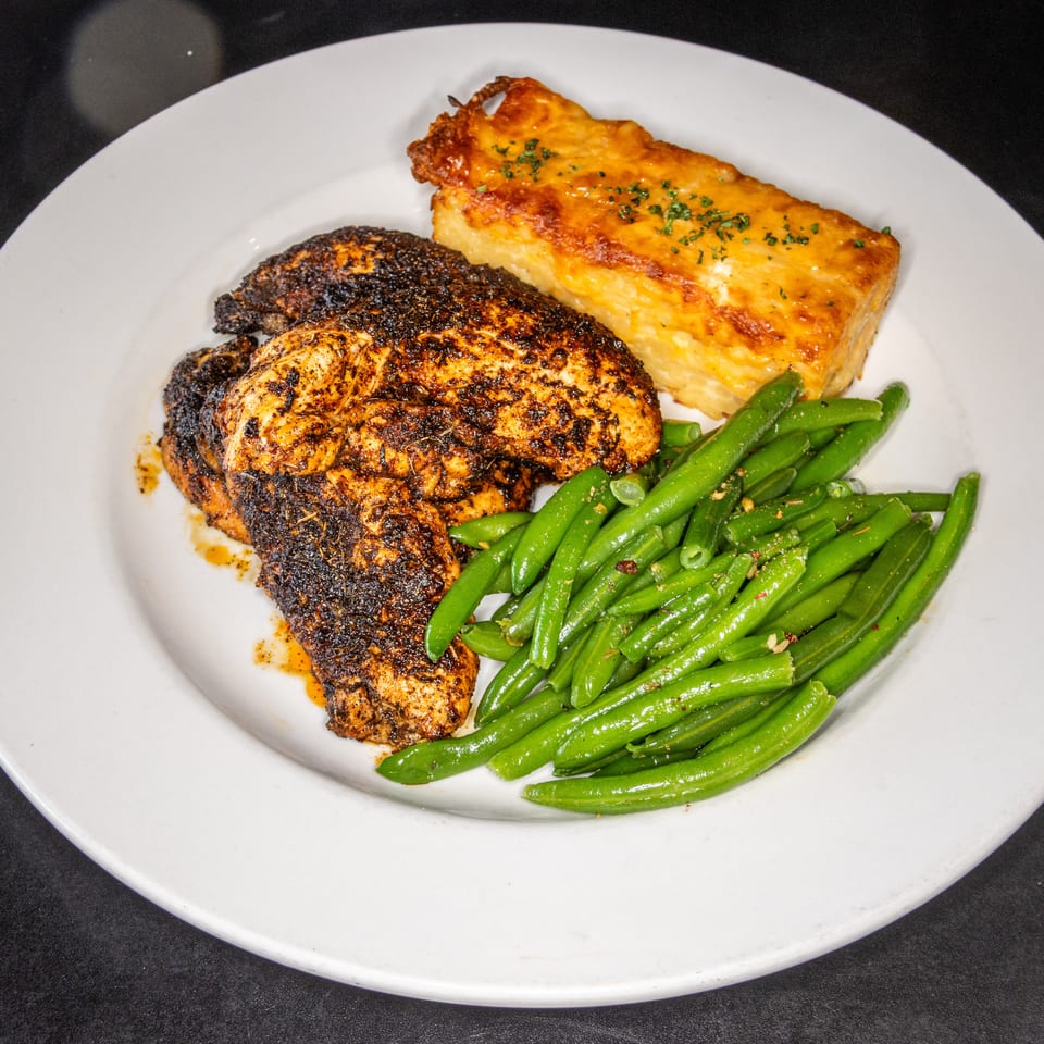 Blackened chicken breast served with green beans and a golden baked macaroni and cheese portion on a white plate.