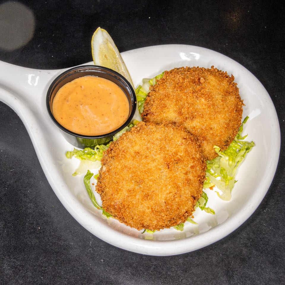 Two golden-breaded patties served over shredded lettuce with creamy orange dipping sauce and a lemon wedge on a white plate.