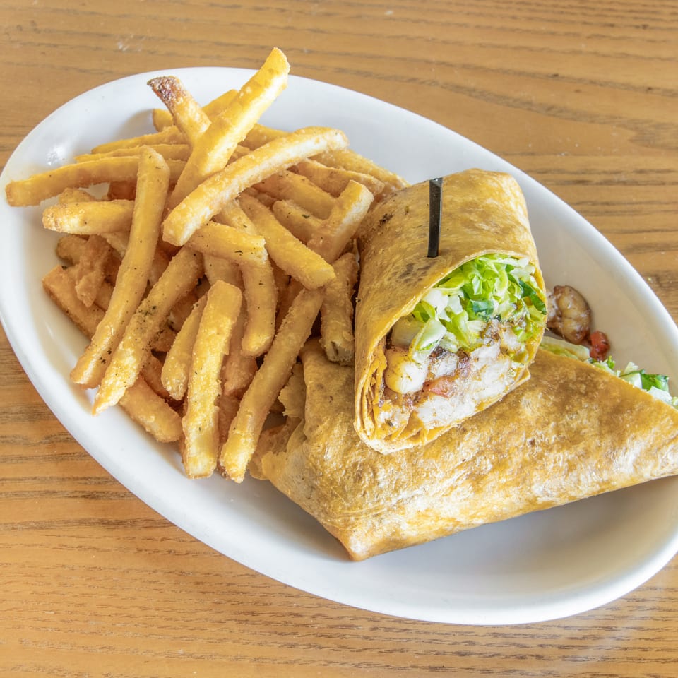 Grilled wrap filled with lettuce and vegetables served with seasoned fries on a white plate.