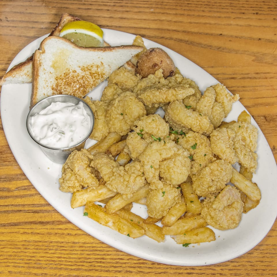 Plate of golden fried seafood and fries with toast, lemon wedges, and creamy dipping sauce on a wooden table.