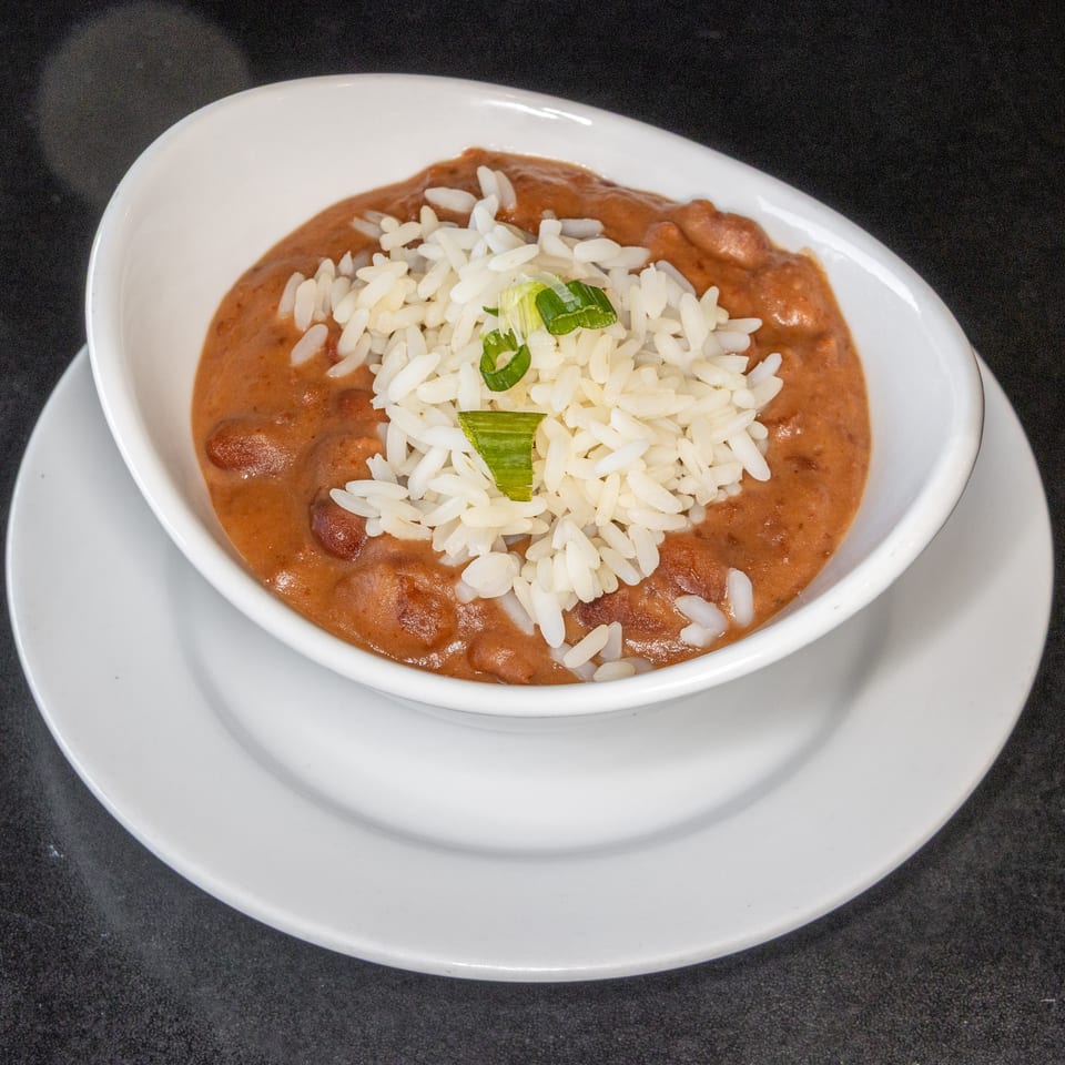 Bowl of creamy red beans topped with white rice and sliced green onions on a white plate.
